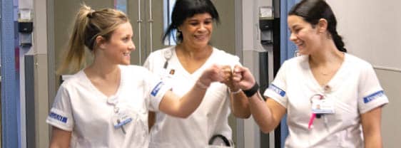 Three nursing student in uniform demonstrating teamwork in a simulation lab.